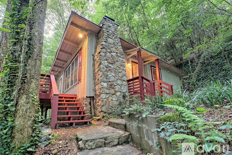 A small house with a stone chimney is surrounded by greenery.