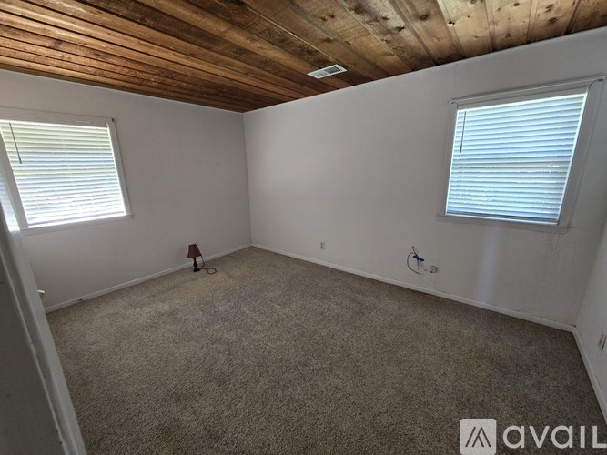 A room with a carpeted floor, wooden ceiling, and two windows with blinds.