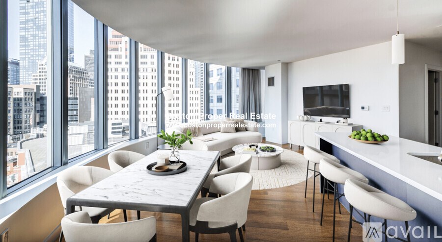 A modern dining room with a long table and chairs, a kitchen area, and a view of the city skyline through large windows.