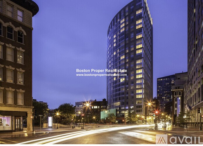 A city street at night with a tall building on the right and a building with a curved facade on the left.