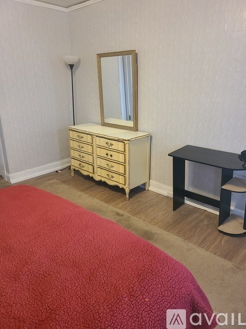 A bedroom with a red bedspread and a wooden dresser with a mirror.