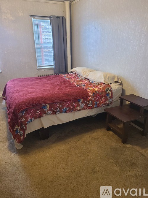 A bed with a red comforter and a small wooden table.