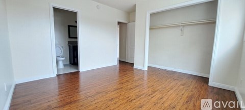 A room with wooden floors and white walls, with a doorway leading to another room.