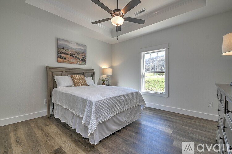 A bedroom with a bed, a ceiling fan, and a painting on the wall.