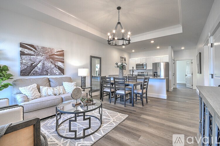 A modern living room with a grey sofa, a glass coffee table, and a chandelier.