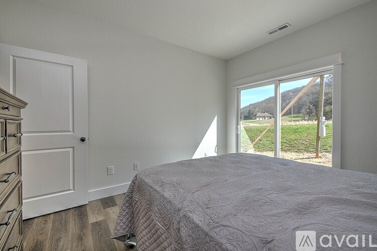 A bedroom with a large bed and a view of the outside through a sliding glass door.