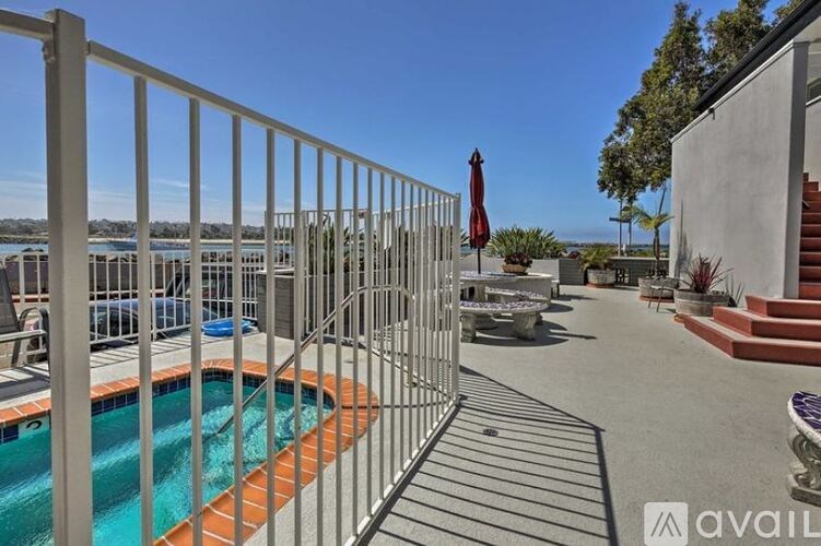 A pool surrounded by a metal fence with a red umbrella in the background.