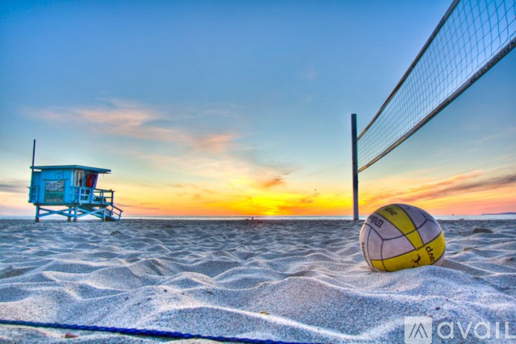 A beach volleyball net and ball on the sand with a lifeguard chair in the background.