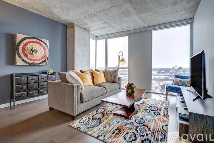 A living room with a grey couch, a large rug, and a TV.