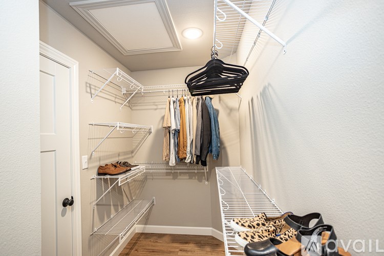 A white closet with clothes hanging and shoes on the shelves.