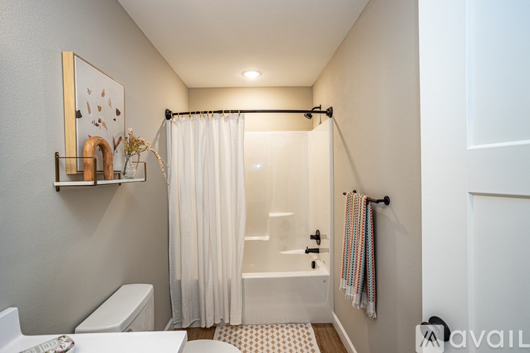 A bathroom with a white toilet, a white bathtub with a shower curtain, a towel rack with a striped towel, and a picture on the wall.