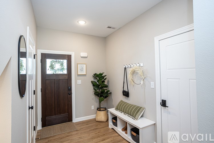 A hallway with a wooden door, a mirror, a bench, and a plant.