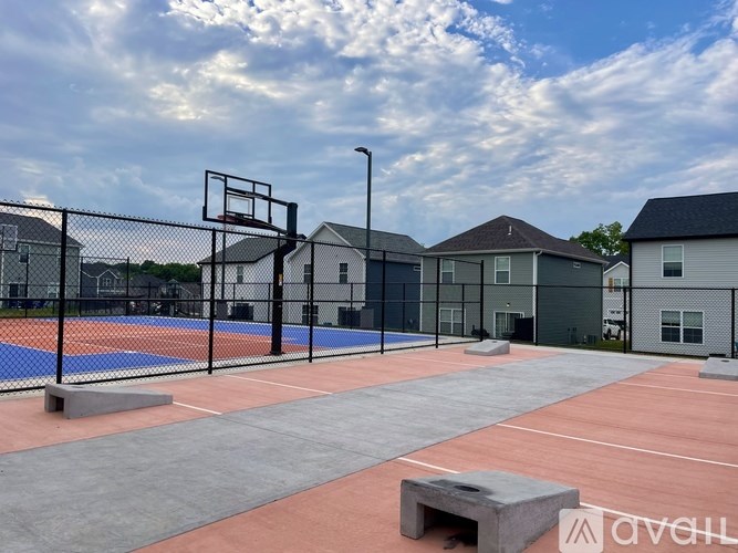 A basketball court is surrounded by a black fence and there are buildings in the background.