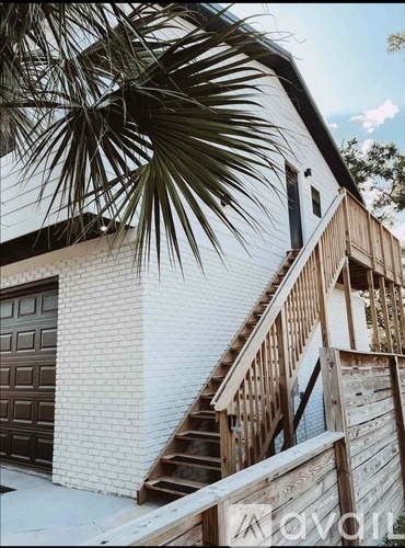 A white house with a wooden staircase and a palm tree in the foreground.