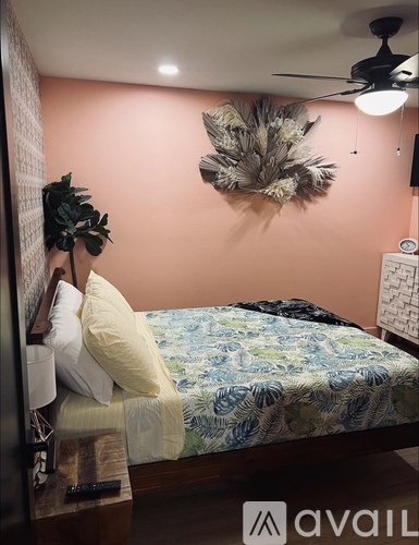 A bedroom with a bed, a ceiling fan, and a wall hanging.