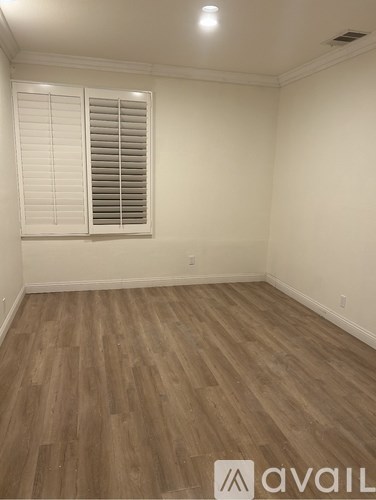 A room with wooden flooring and a window with blinds.