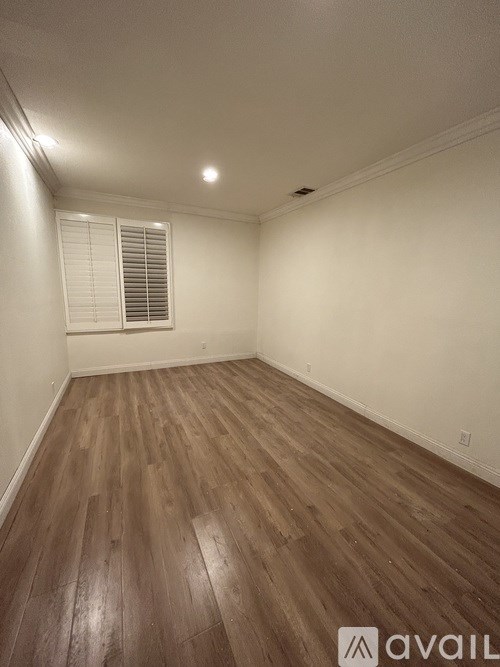 A room with wooden flooring and a window with blinds.