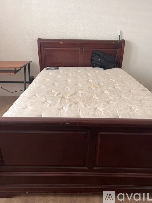 A bed with a wooden headboard and footboard with a white mattress and a black bag on the pillow.
