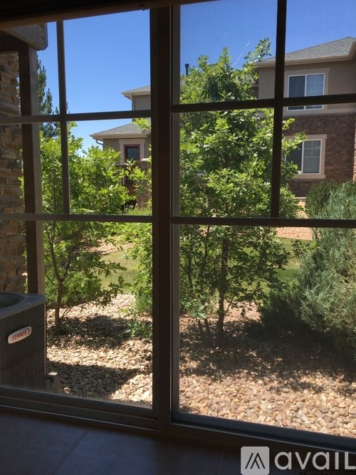 A view from inside a house looking out through a window at a garden with a brick house in the background.