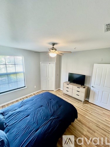 A bedroom with a bed covered in a blue sheet, a ceiling fan, and a television on a cabinet.