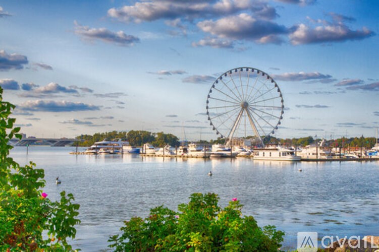 A ferris wheel is in the background of a body of water with boats and buildings.