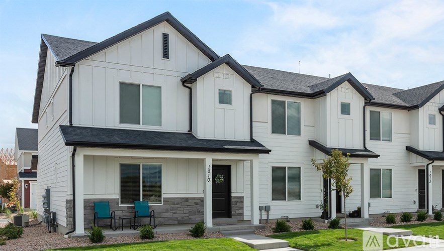 A modern house with a black front door and two green chairs on the porch.