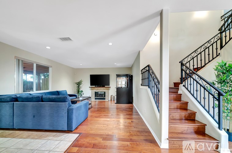 A living room with a blue couch and a staircase with a black railing.