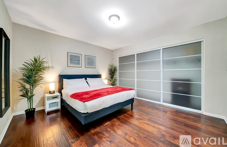 A bedroom with a bed, nightstand, and two potted plants.