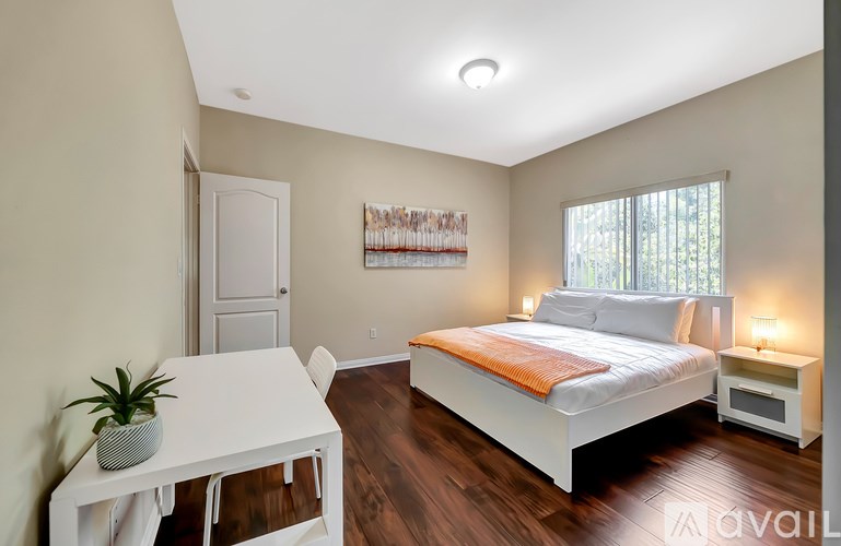 A bedroom with a white bed and a white table with a plant on it.