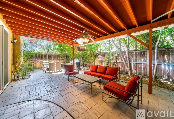 A patio with a red couch and chairs under a wooden pergola.