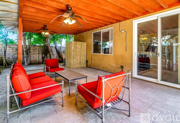 A patio with red chairs and a ceiling fan.