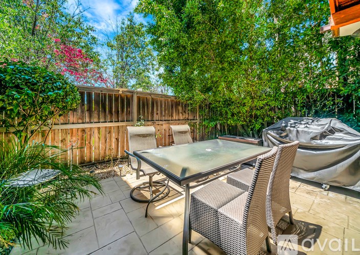 A patio with a glass table and chairs surrounded by greenery.