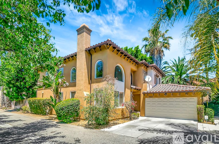 A house with a brown roof and a white garage door is surrounded by greenery.