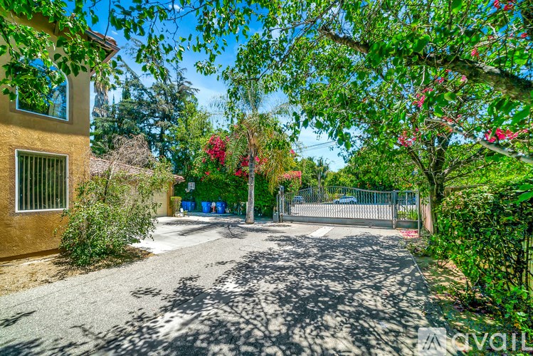 A gravel driveway leads to a house with a gate and a tree with pink flowers.