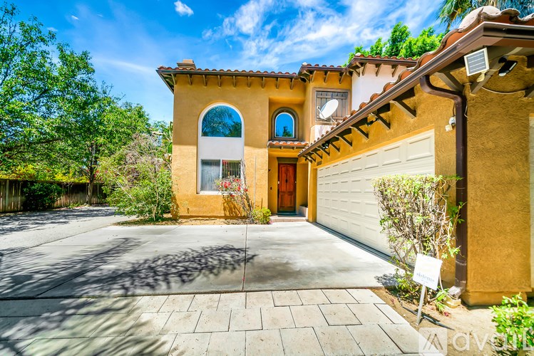 A house with a brown facade and a red door is surrounded by greenery.