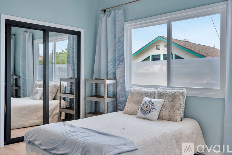 A bedroom with a bed, pillows, and a window overlooking a house.