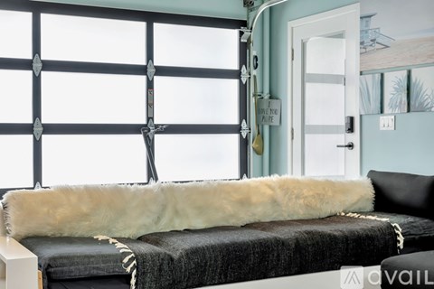 A bedroom with a bed covered in a black blanket and a white fur throw.