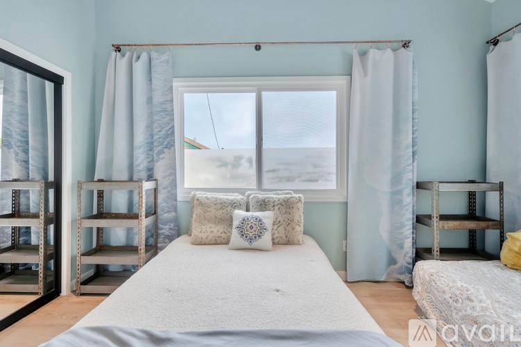 A bedroom with a bed, two shelves, and a window with curtains.