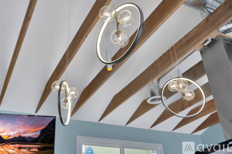 A modern chandelier hangs from a ceiling with wooden beams.