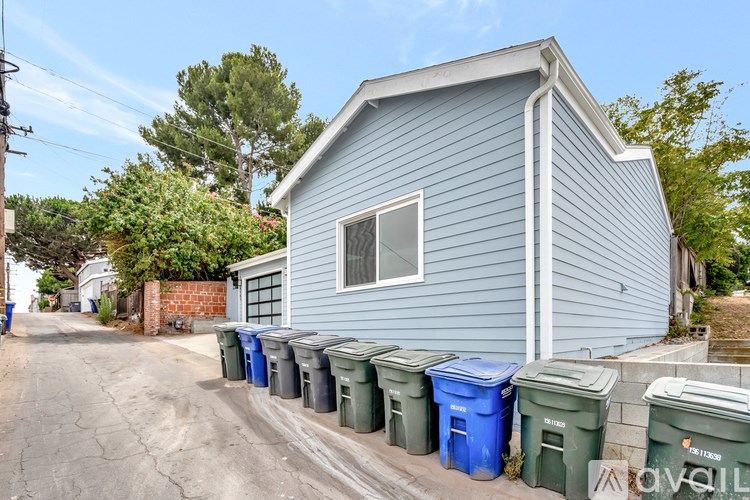 A blue house with a white window and a row of trash bins in front.