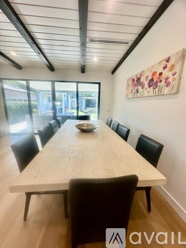 A long wooden table is surrounded by black chairs in a room with a large painting on the wall.