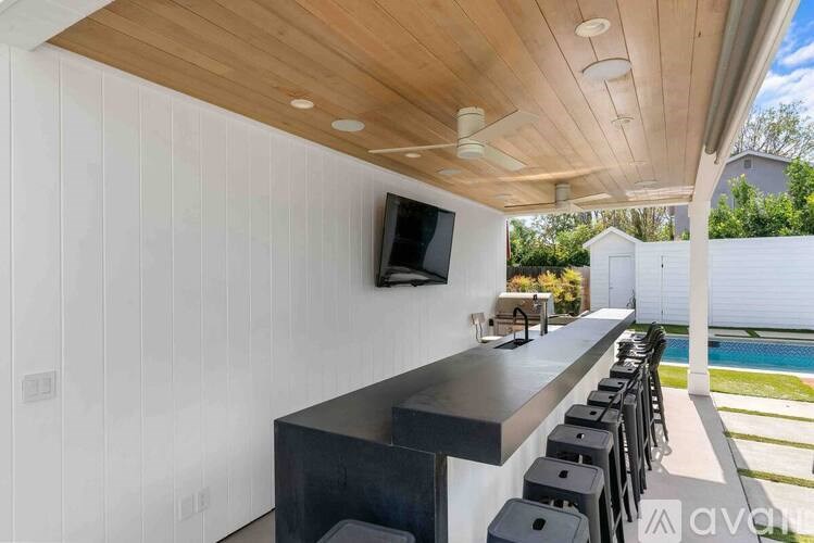 A modern outdoor kitchen with a long bar and black stools.