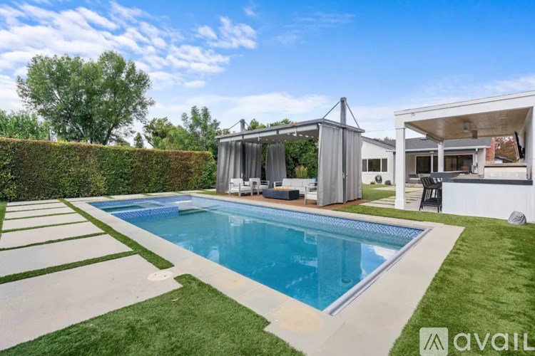 A swimming pool in a backyard with a hedge and a house in the background.