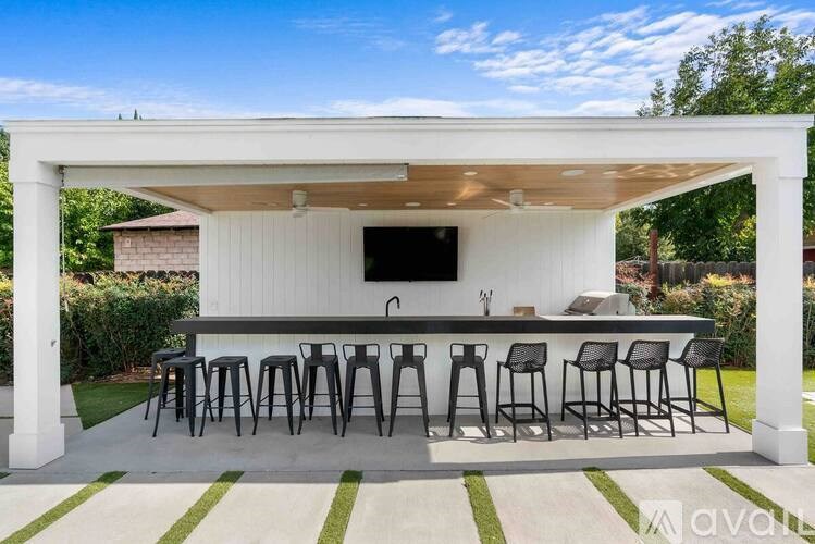 A white outdoor bar area with a television and black stools.