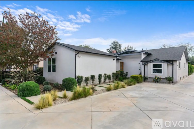 A modern house with a white exterior and a black roof is surrounded by a well-maintained garden.