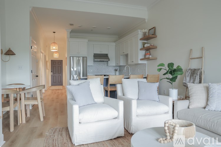 A living room with white furniture and a kitchen in the background.