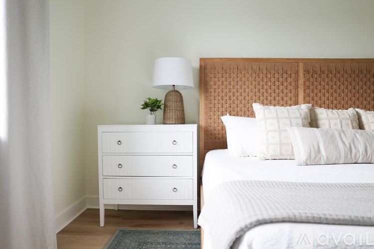 A white bedroom with a bed, nightstand, and lamp.