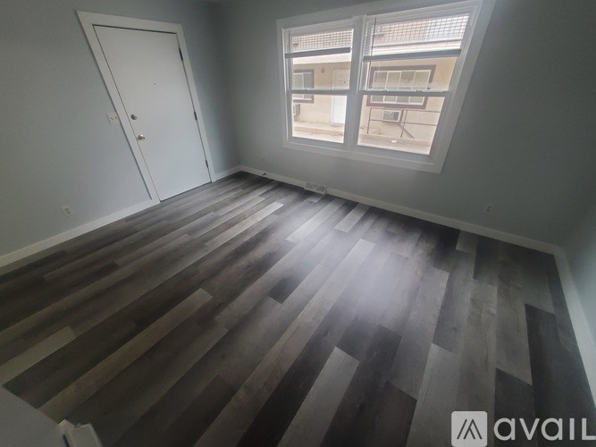 A room with a wooden floor and a window showing a balcony.