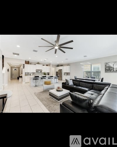 A modern living room with a black leather sofa and a ceiling fan.