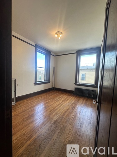A room with wooden flooring and two windows.